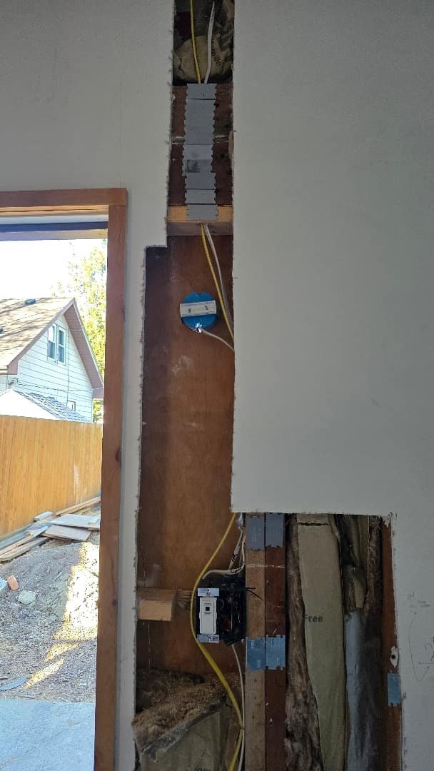 Partially finished wall with installed electrical wiring, outlet box, and breaker panel in a residential construction site.