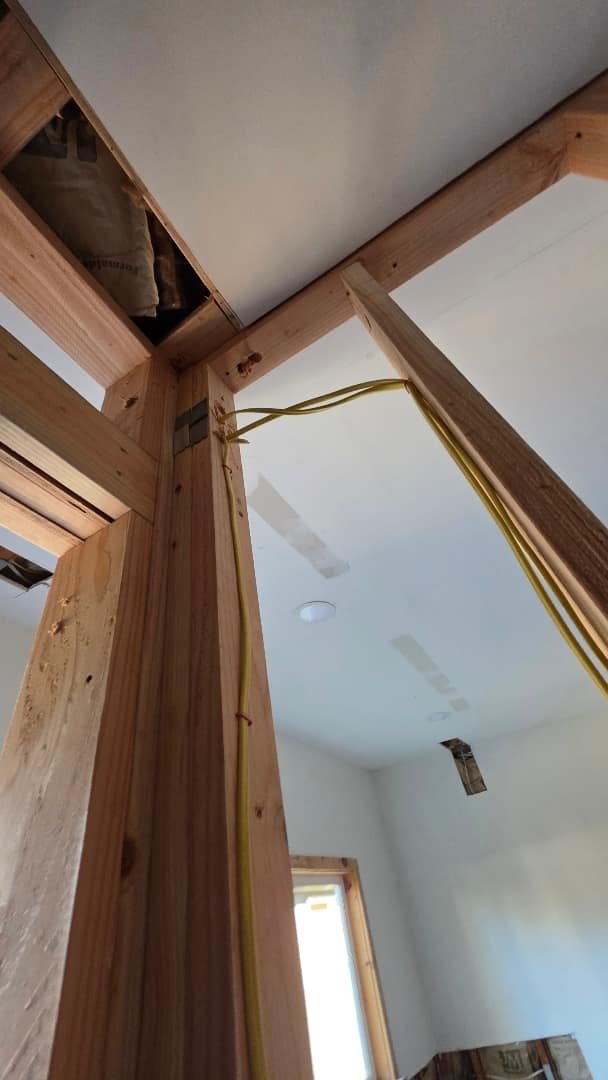 Exposed wiring running through wooden framing in a residential construction context.