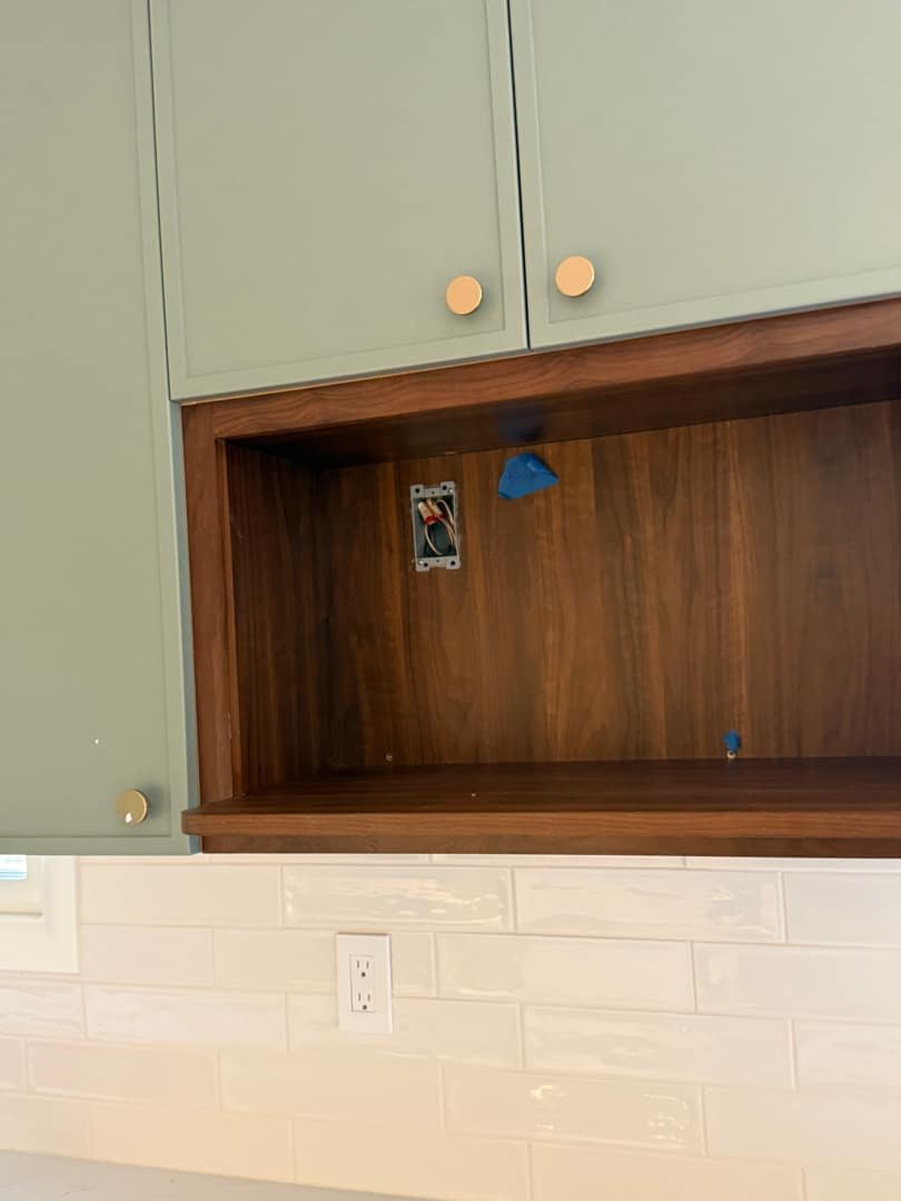 A partially installed electrical outlet box with blue painter's tape, showing in-progress wiring inside a cabinet.
